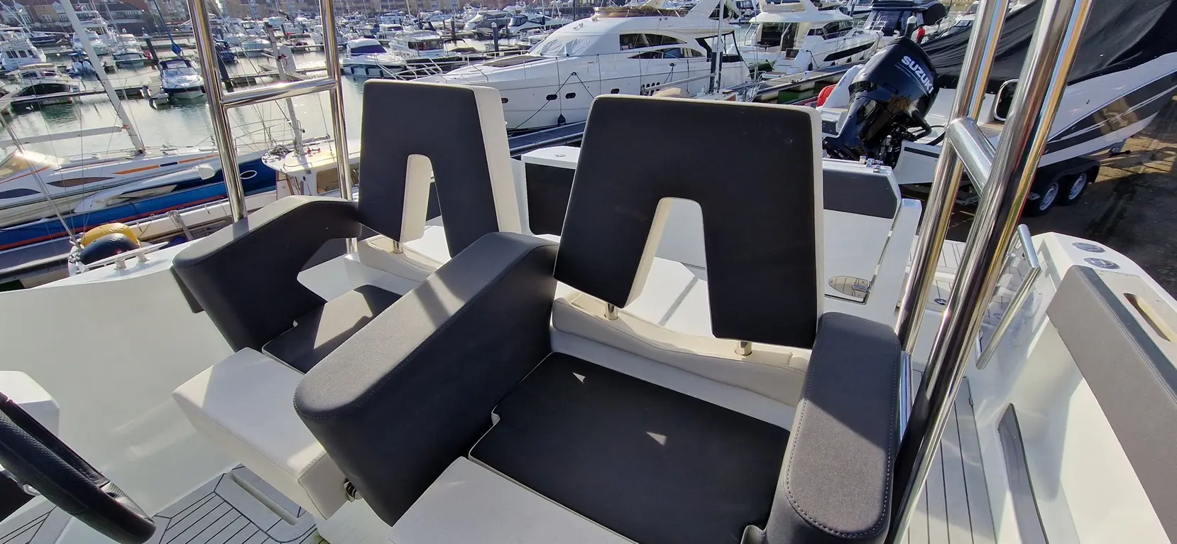 Two black padded boat seats are positioned near the edge of a yacht, overlooking a bustling marina filled with luxury boats.